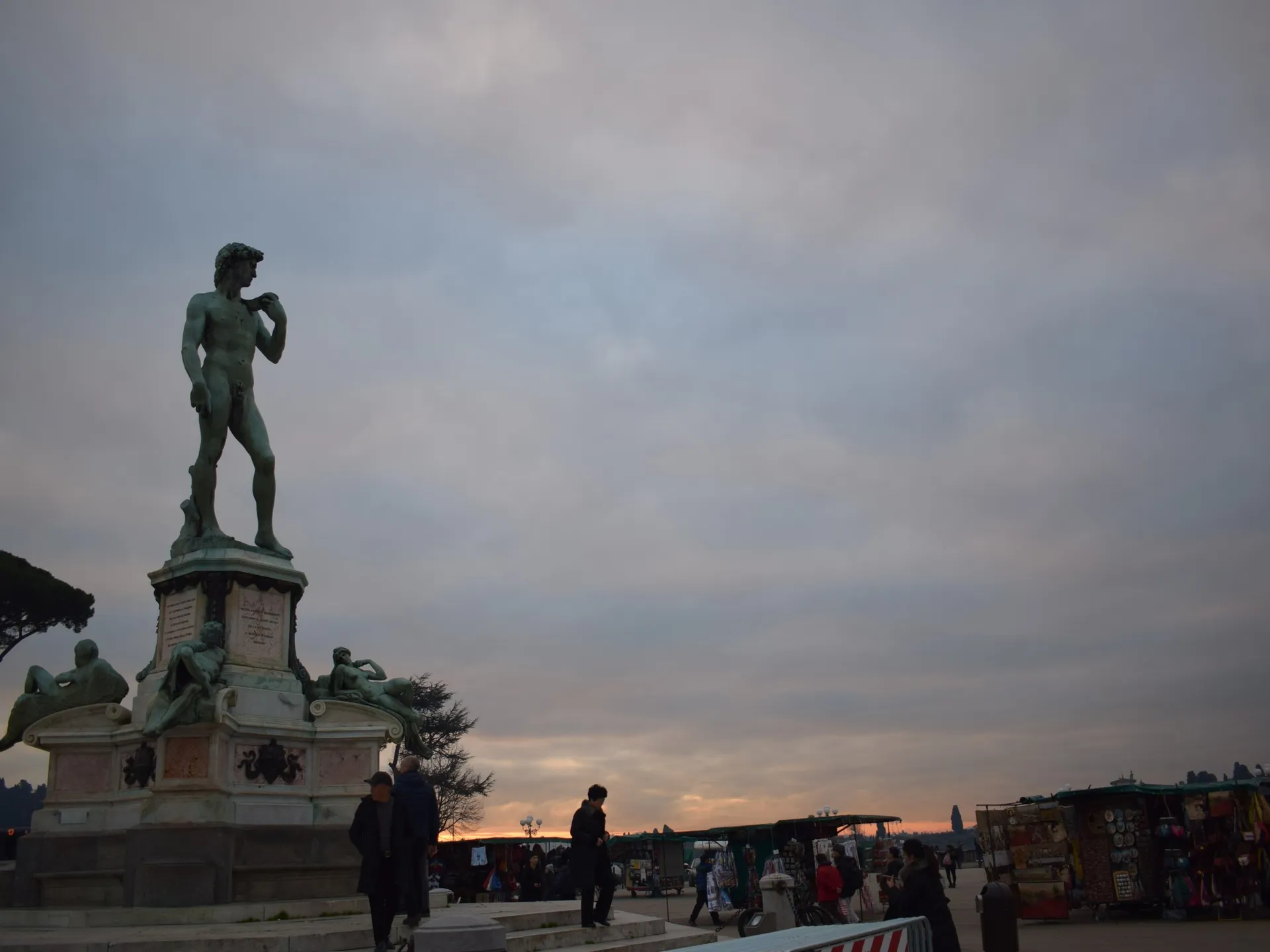 Bronze replica of Michelangelo's David at Piazzale Michelangelo at dusk, with souvenir stalls and Florence beyond