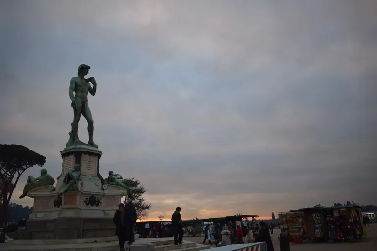Bronze replica of Michelangelo's David at Piazzale Michelangelo at dusk, with souvenir stalls and Florence beyond
