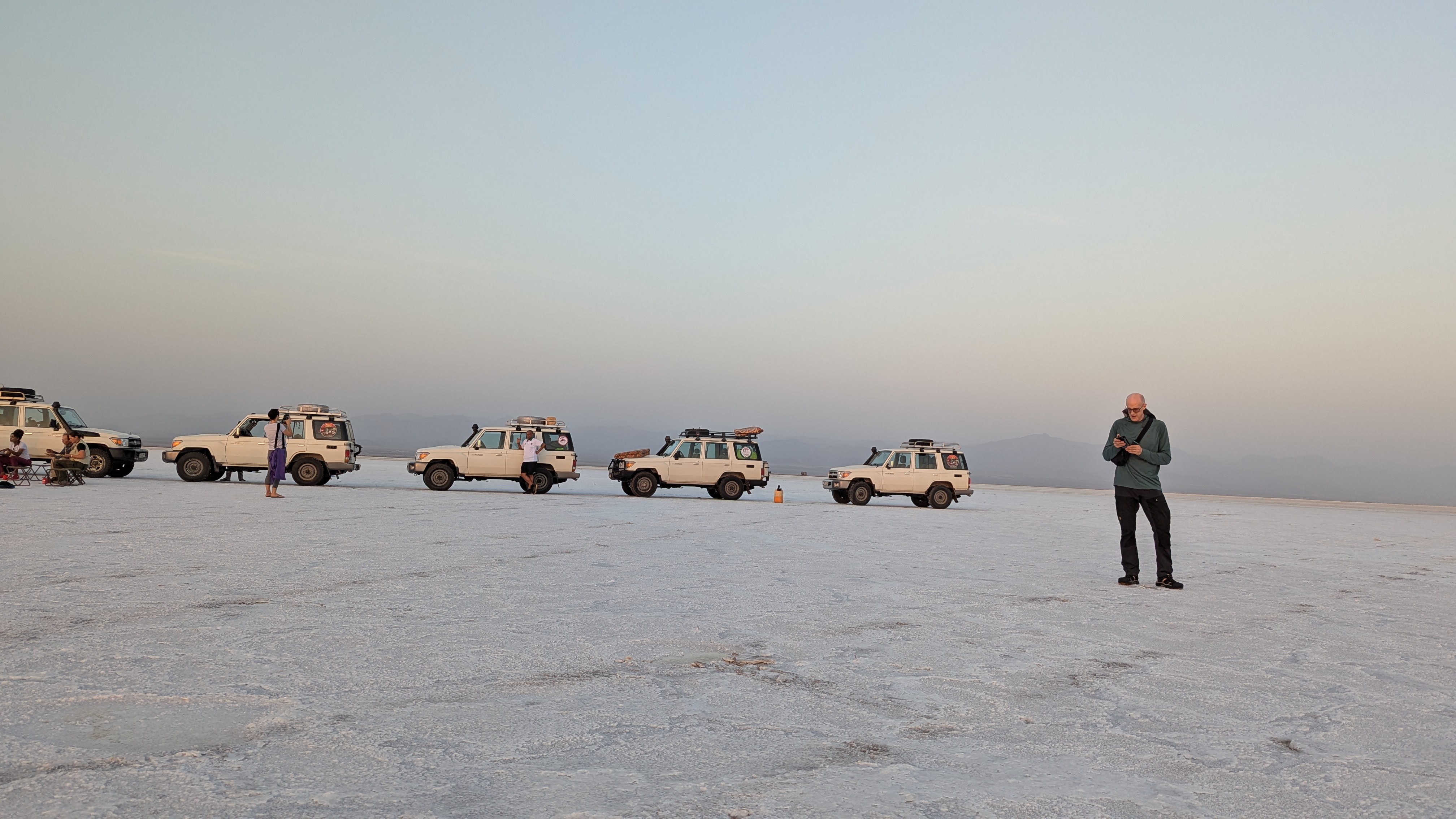 Expedition vehicles and a traveler on a wide salt flat at dusk