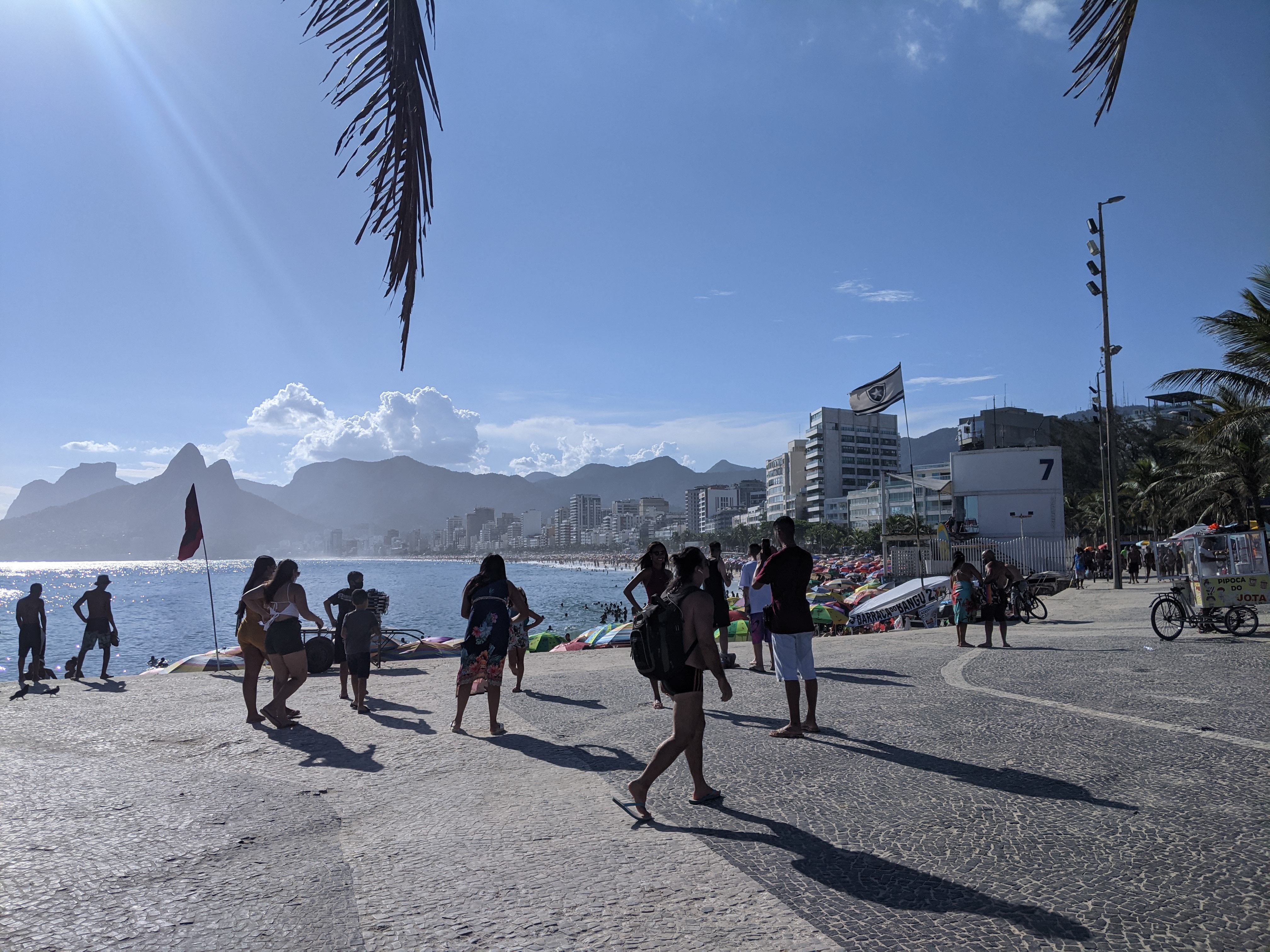 People walking the Arpoador promenade with Dois Irmãos mountain rising behind the beach