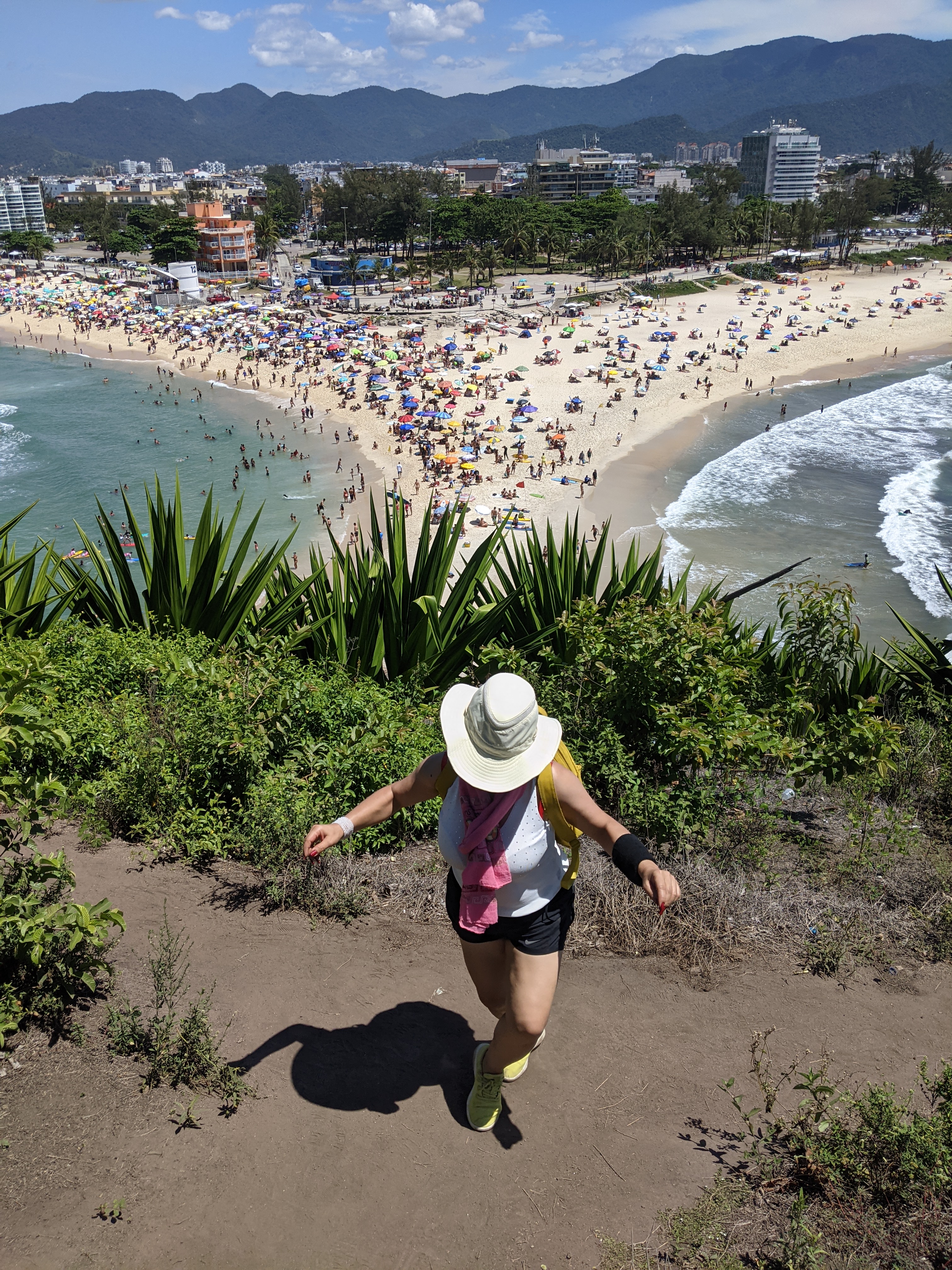 Walker on a clifftop trail above a crowded crescent beach near Rio de Janeiro