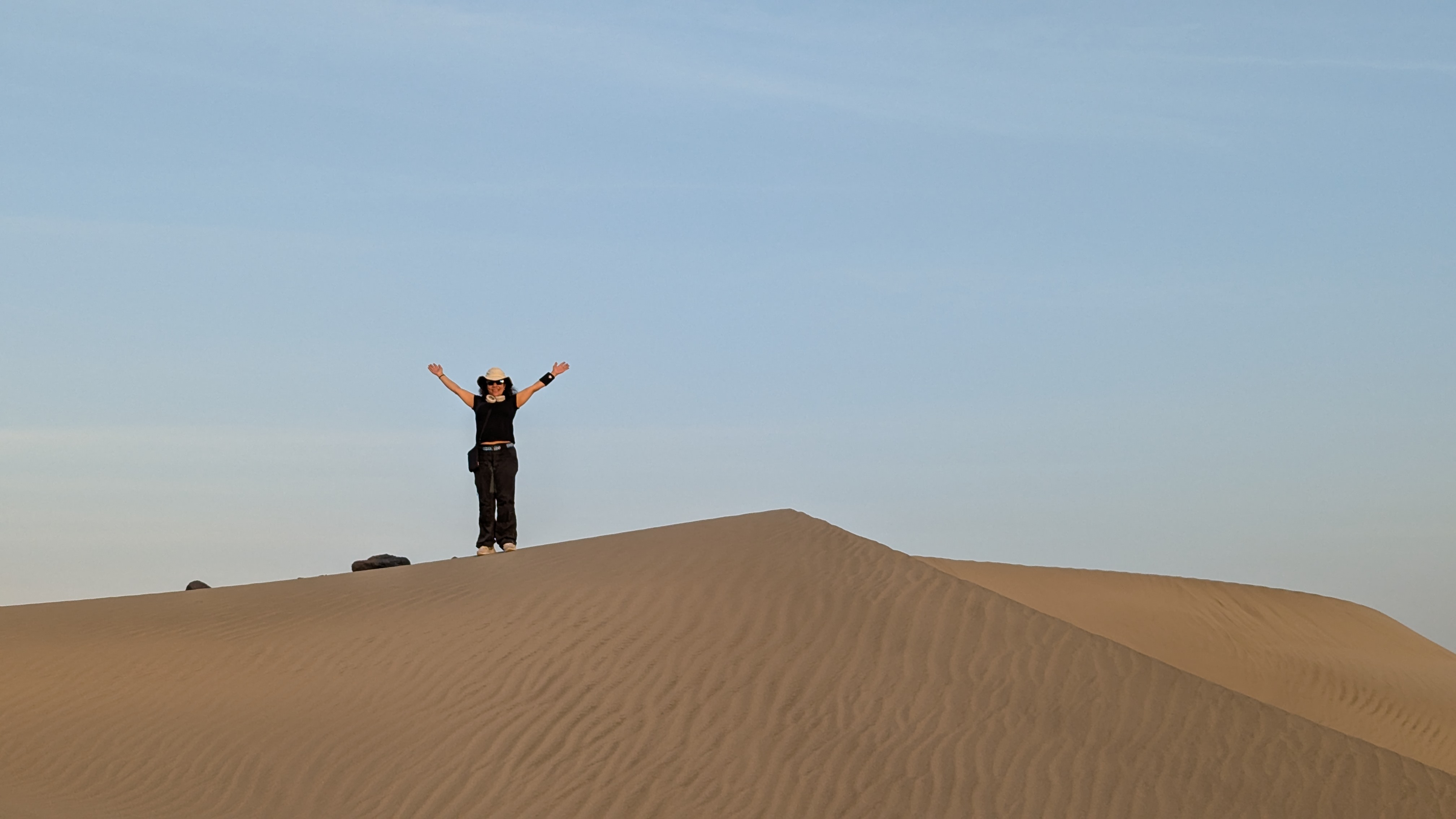 Traveller standing with arms raised on a sand dune ridge at dusk in the Afar desert