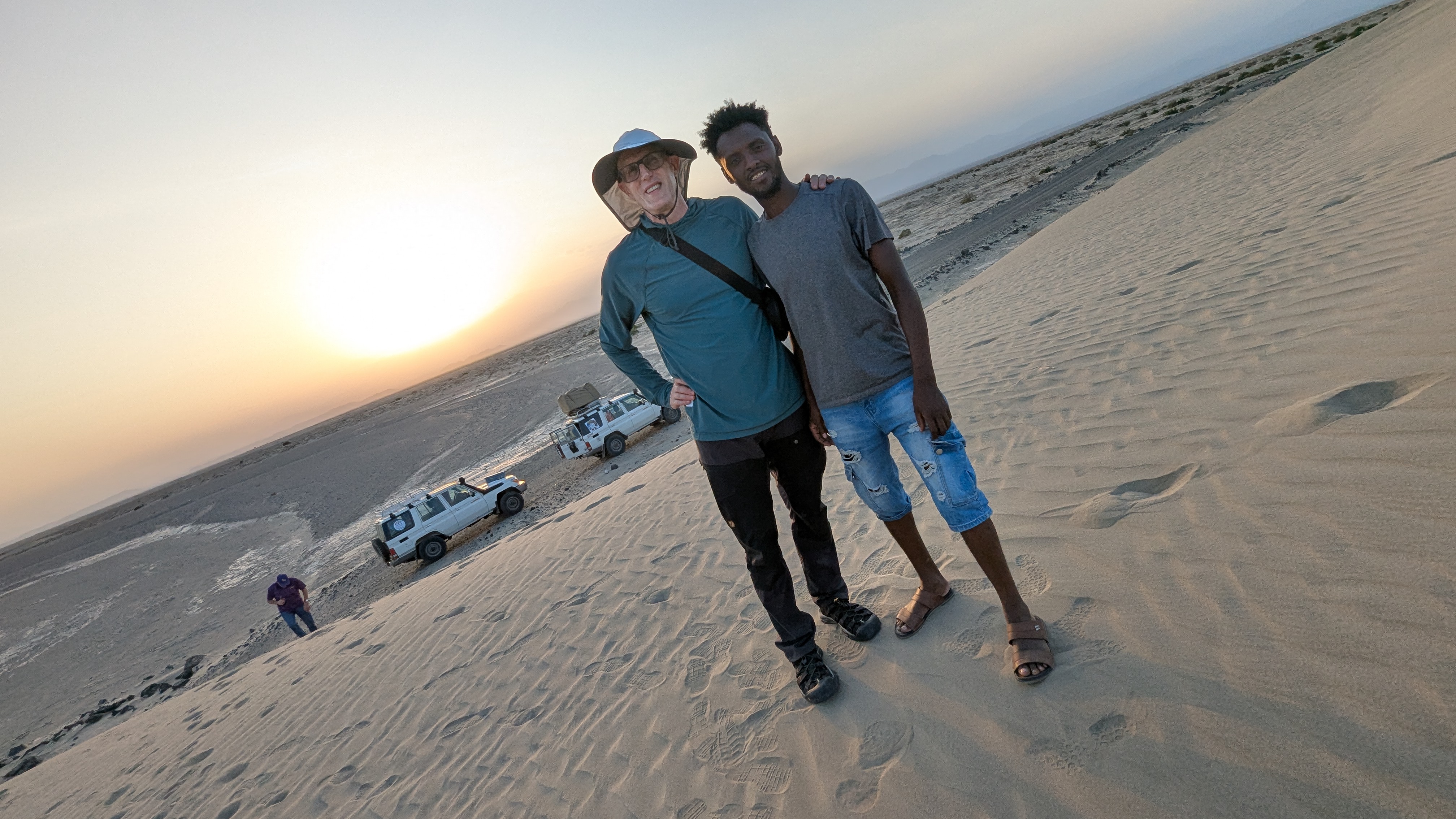 Travellers and a local guide beside 4x4 Land Cruisers on the salt flats at sunset