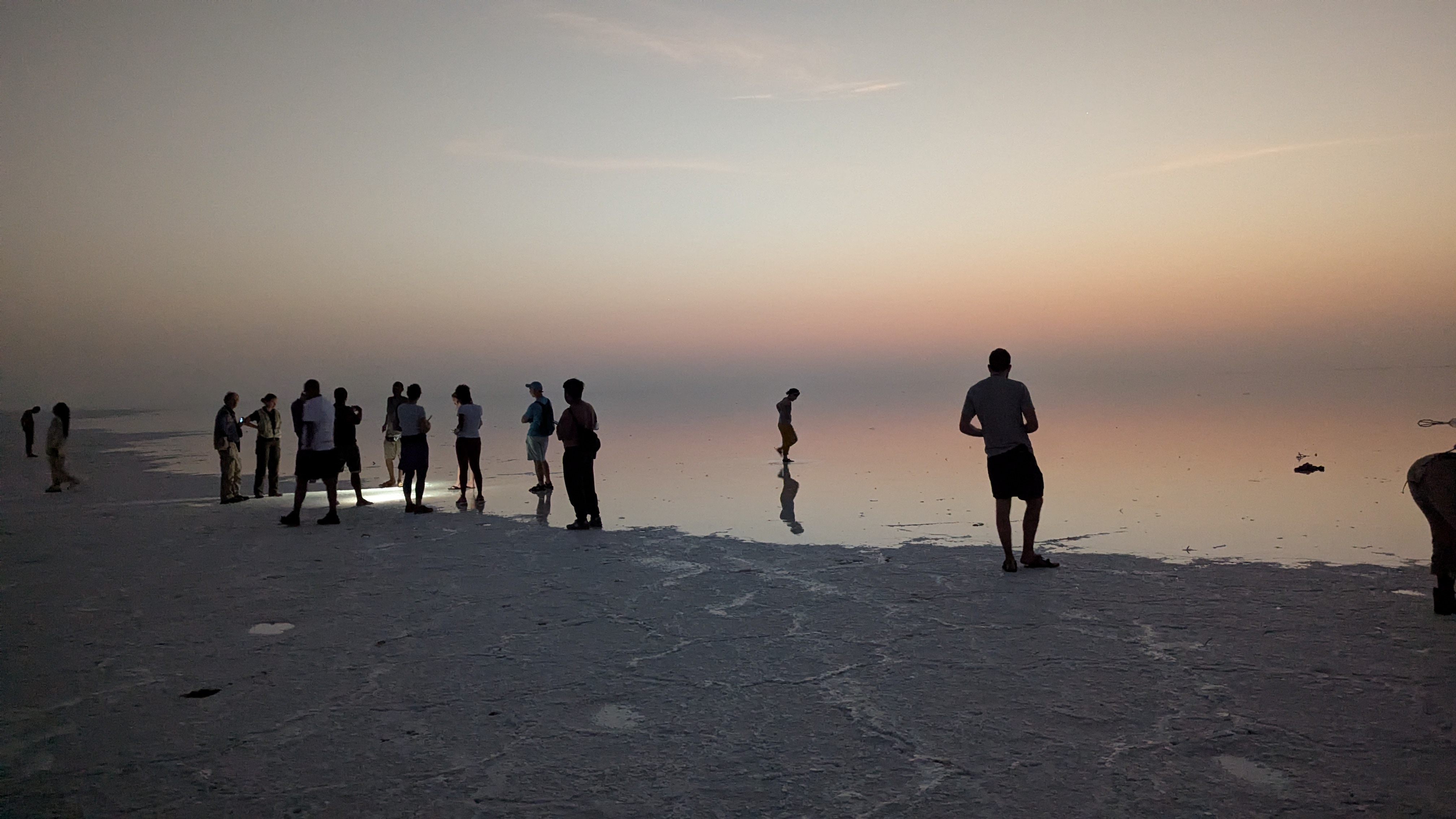 Tourists silhouetted on the Danakil salt flats at sunset with reflections in a thin layer of water