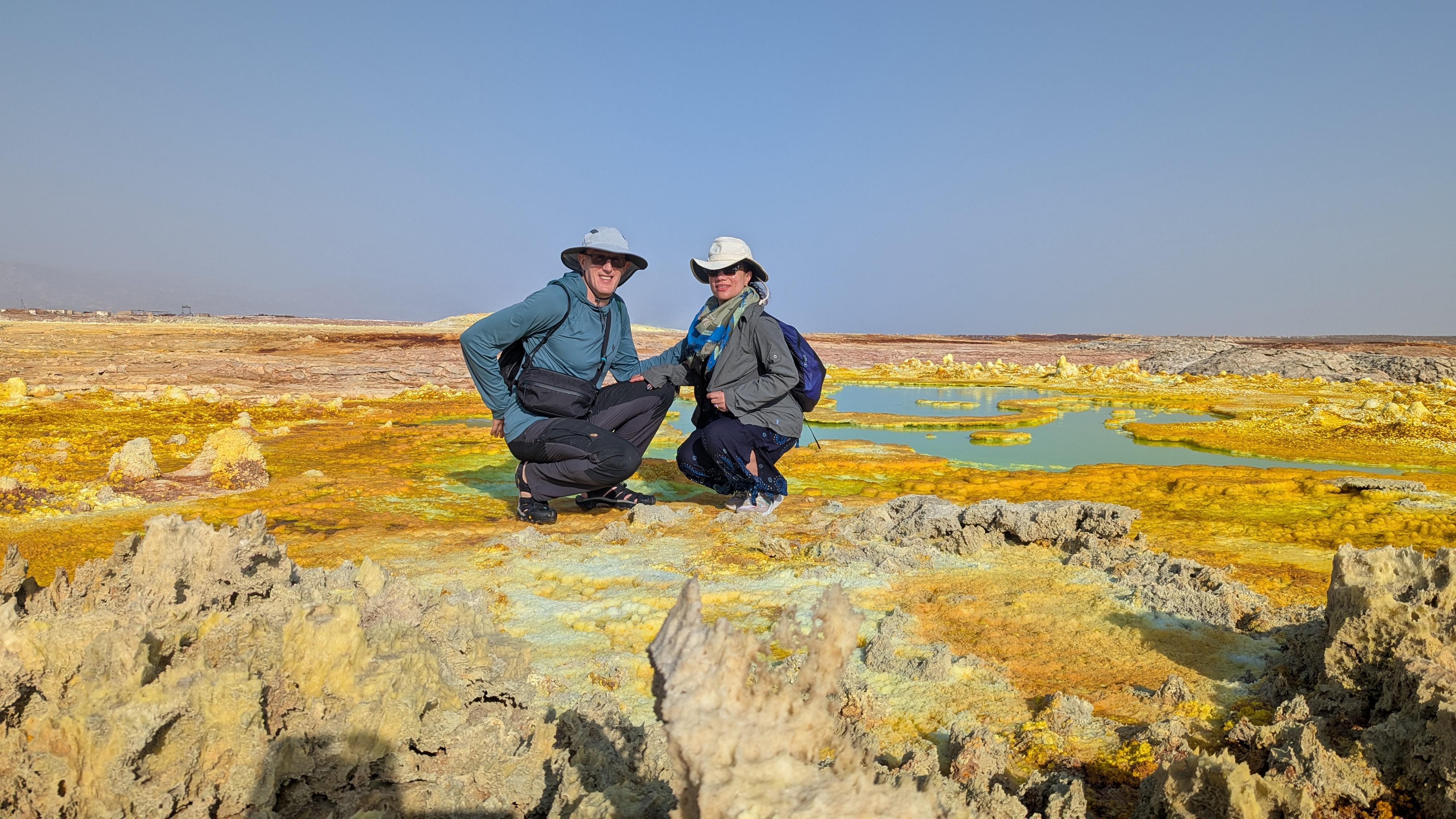 Two travellers crouching among the yellow and green sulphur formations of Dallol
