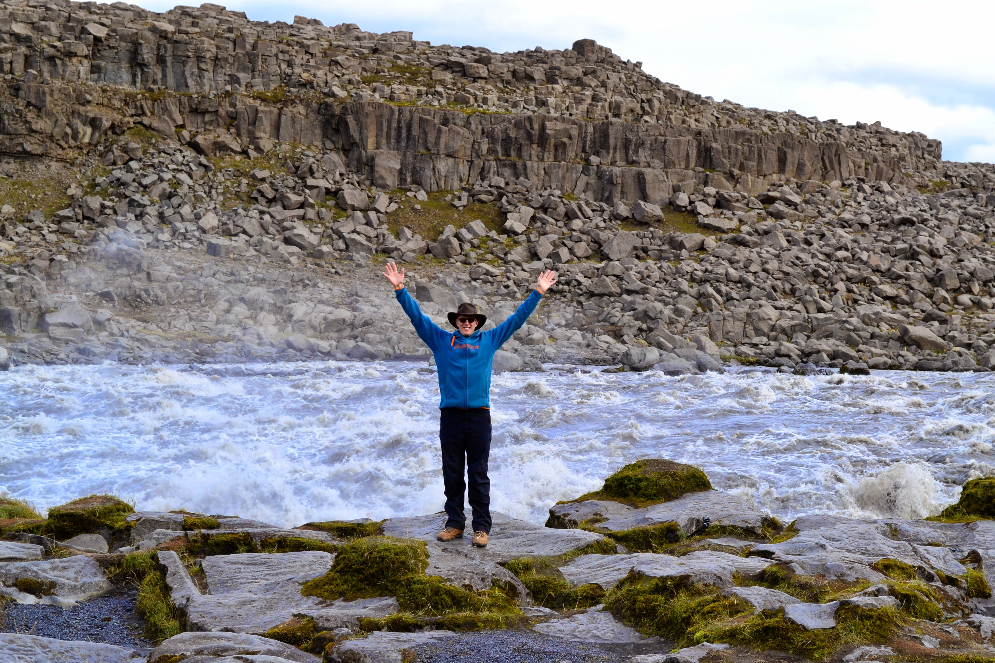 Visitor standing near turbulent glacial water and basalt rocks at Dettifoss