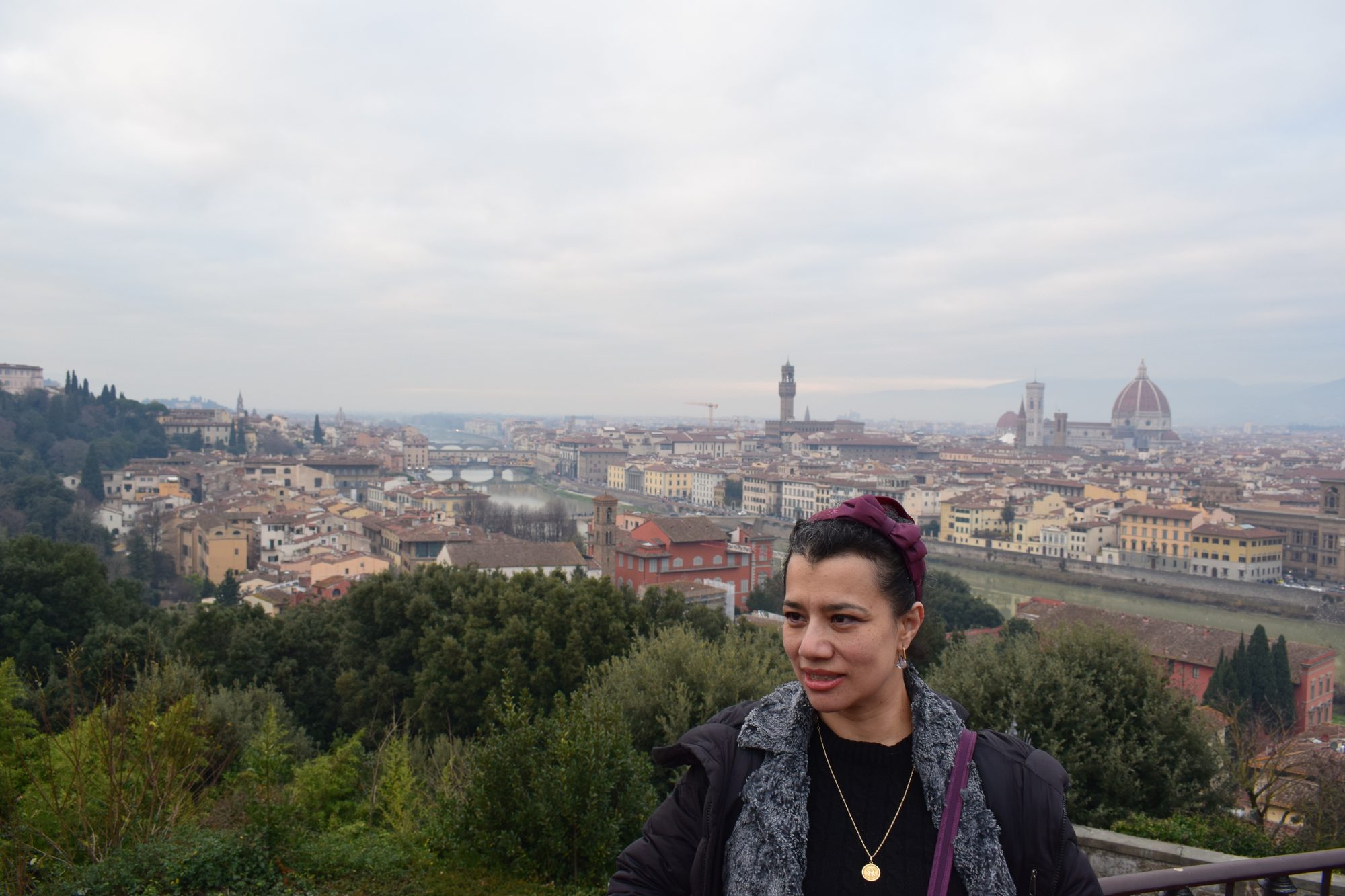 Traveller at the Piazzale Michelangelo viewpoint with the Florence skyline, Duomo and Palazzo Vecchio tower behind under a grey sky