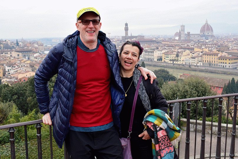 Two travellers smiling at the Piazzale Michelangelo railing with the Duomo and Palazzo Vecchio behind