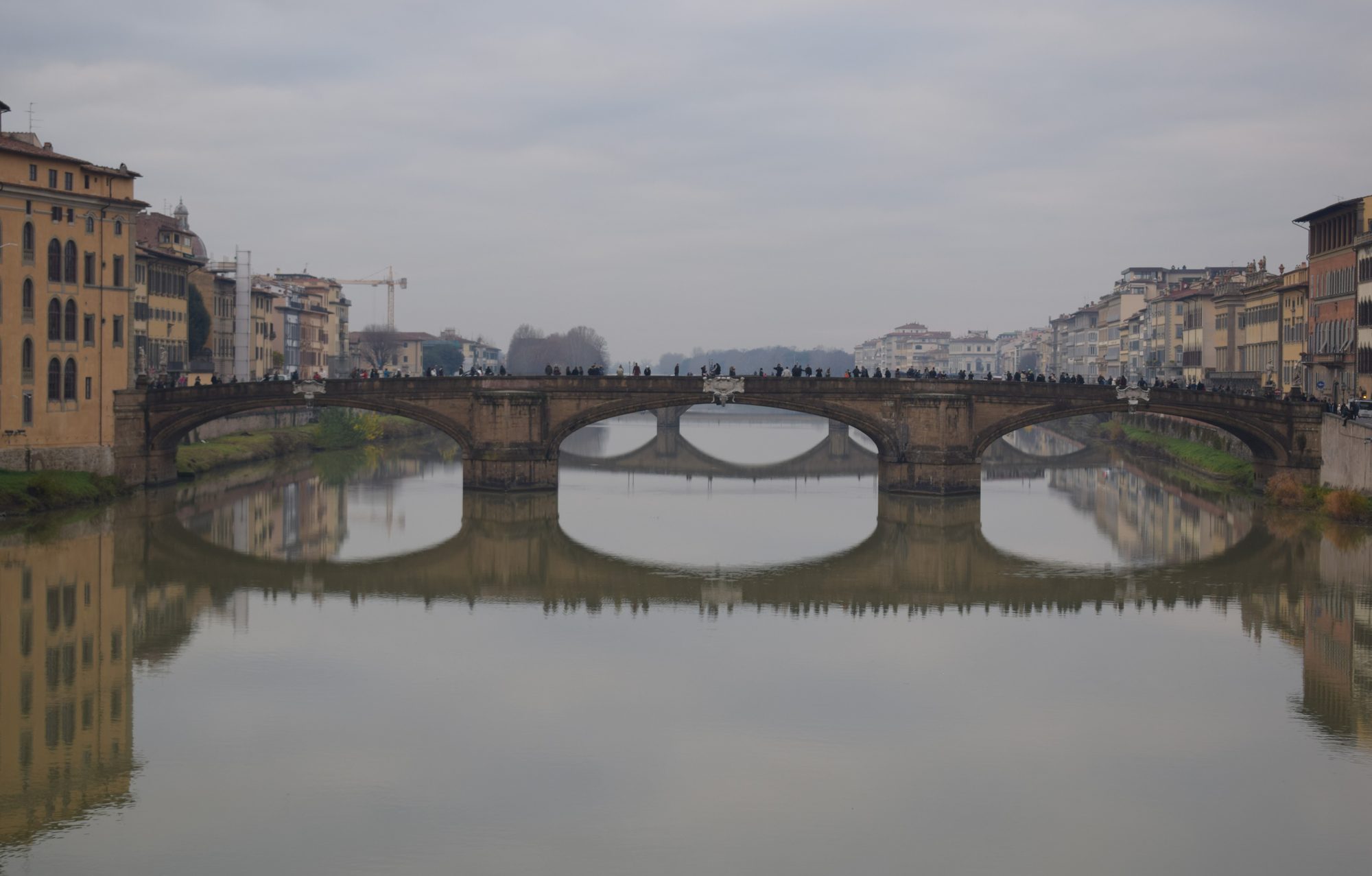 The arched Ponte Santa Trinita reflected in the still water of the Arno with honey-coloured riverside buildings