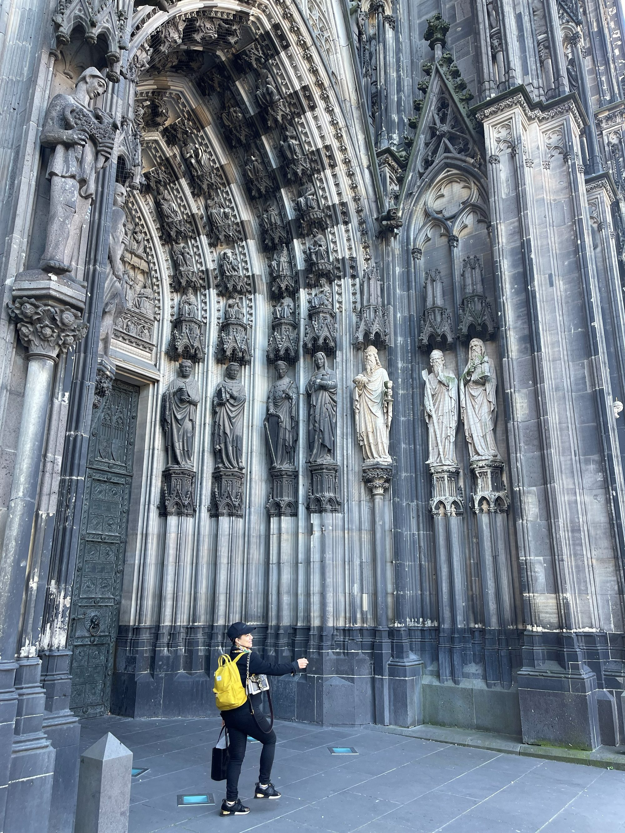 Visitor looking up at the carved Gothic main portal of Cologne Cathedral with rows of saint statues