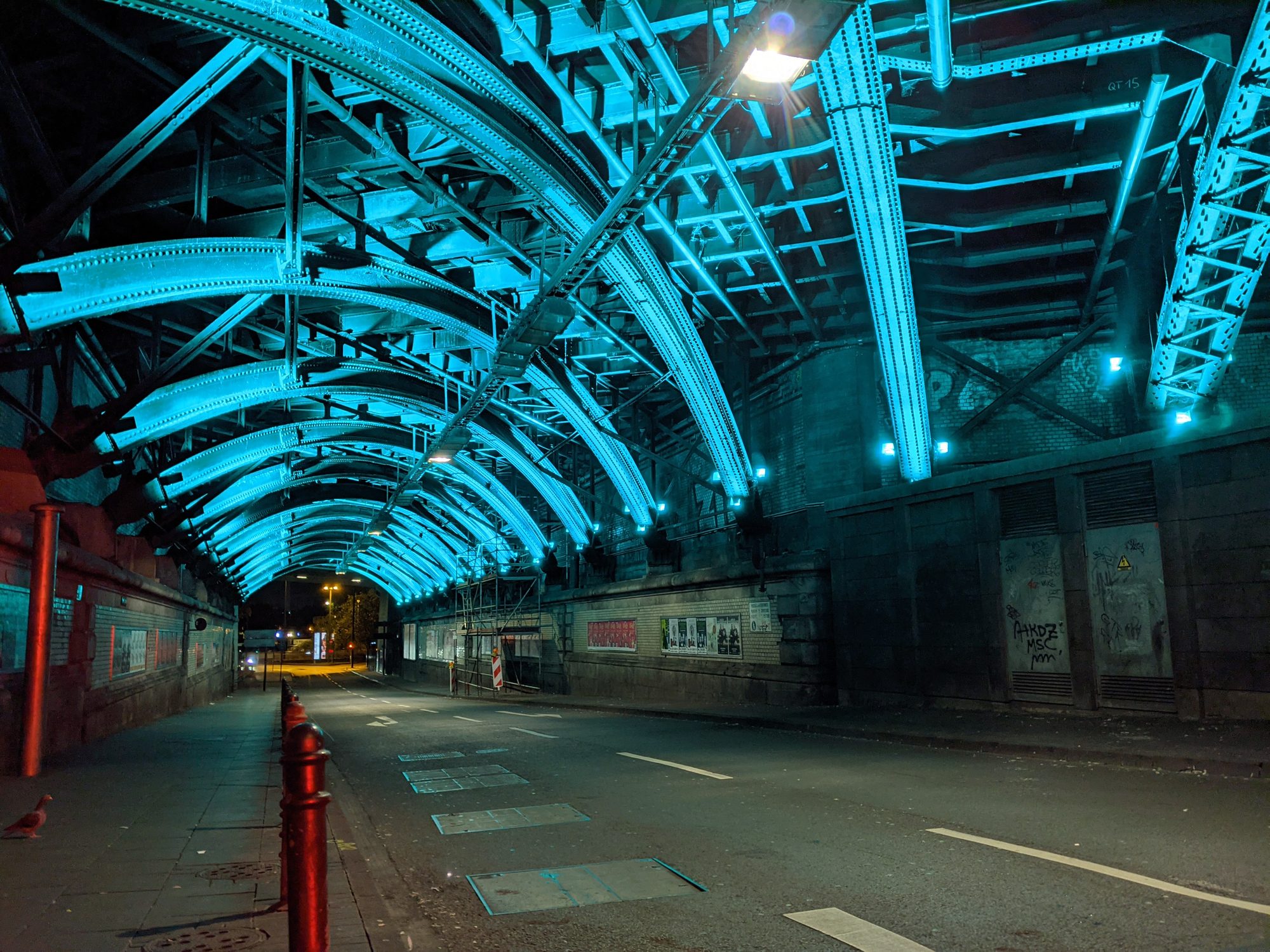 Blue-lit steel girder railway underpass at night in Cologne