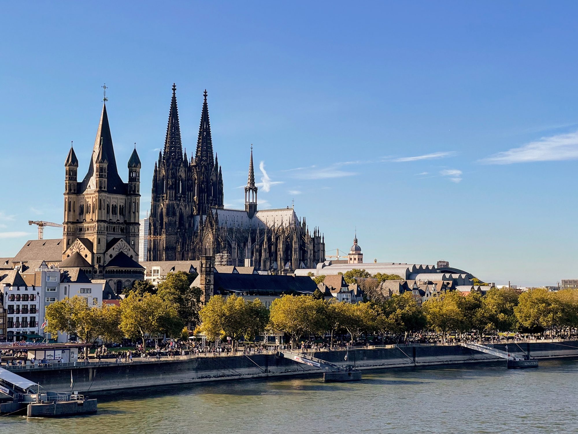Cologne Cathedral and the Romanesque Great St Martin Church above the Rhine waterfront under a blue sky