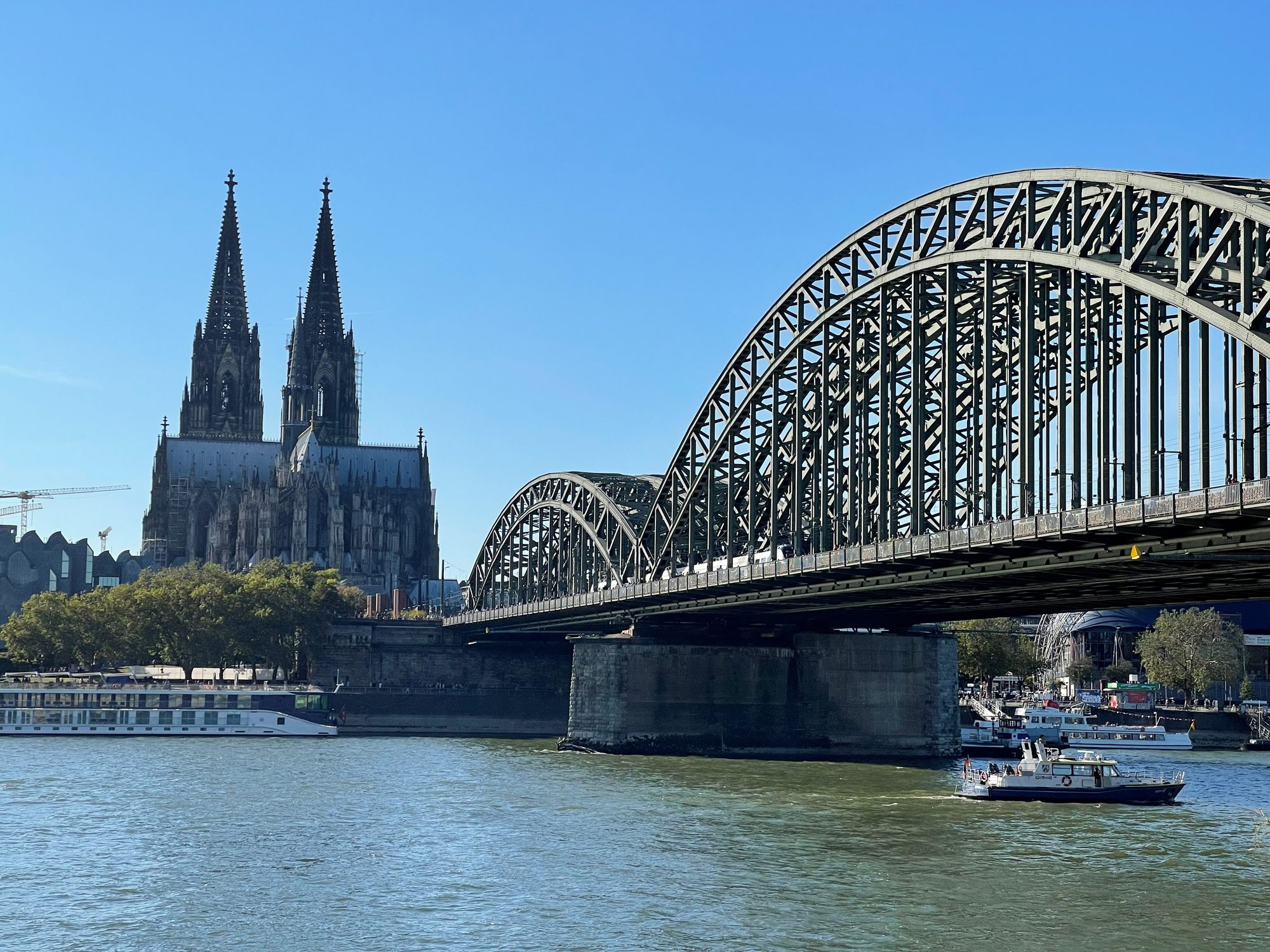 Cologne Cathedral's twin spires beside the arched Hohenzollern Bridge over the Rhine with a river cruise boat
