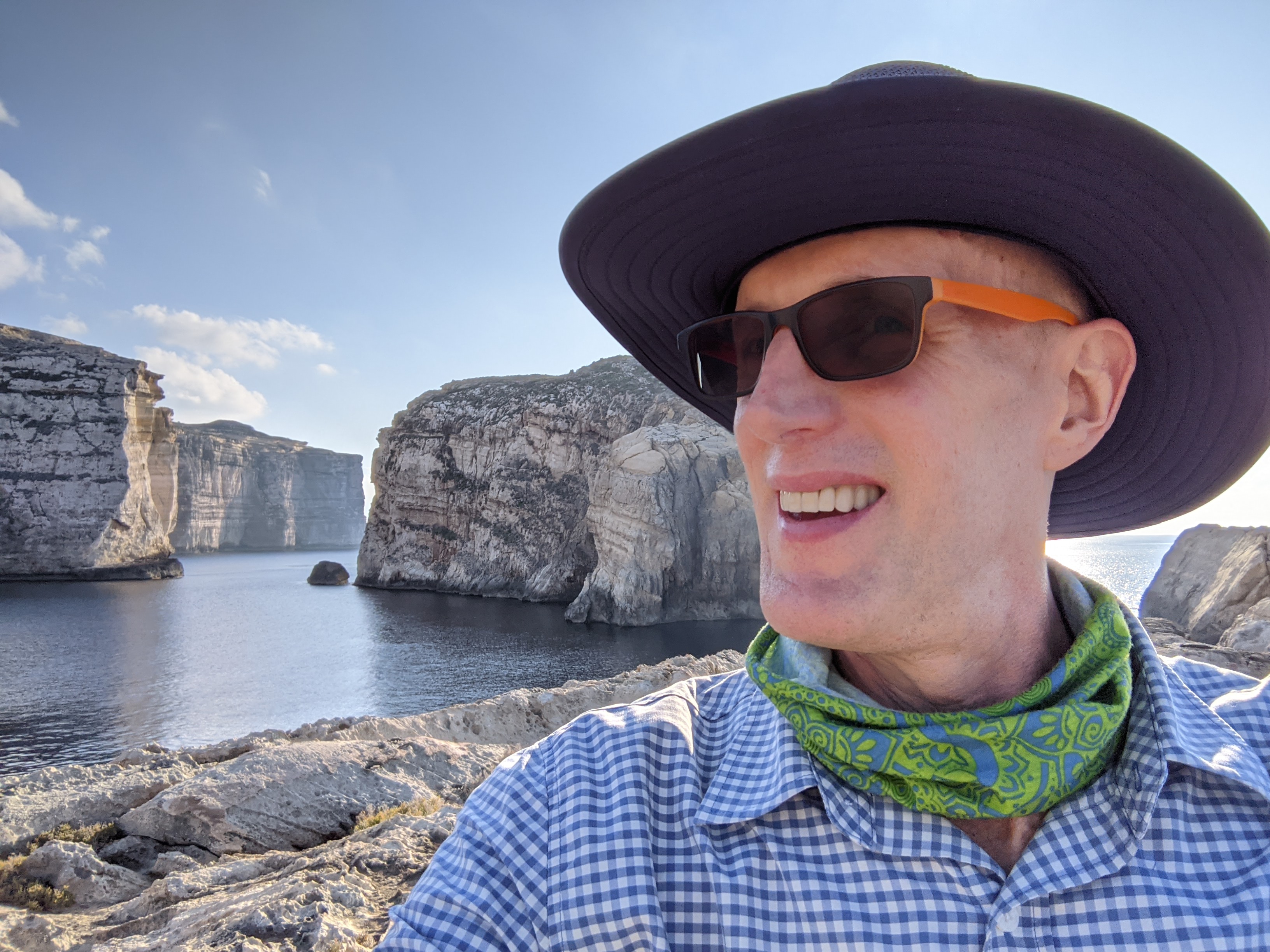 Traveler at Malta's coastal cliffs with blue sea and limestone formations behind